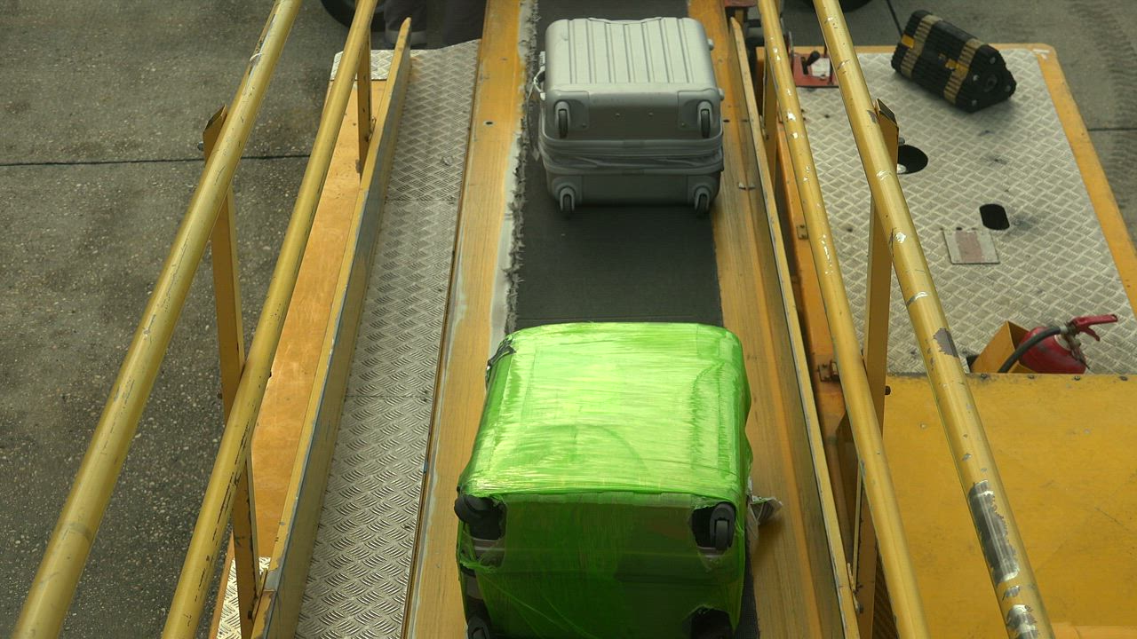 Wrapped and plain suitcases riding a conveyor loader on an airport ramp