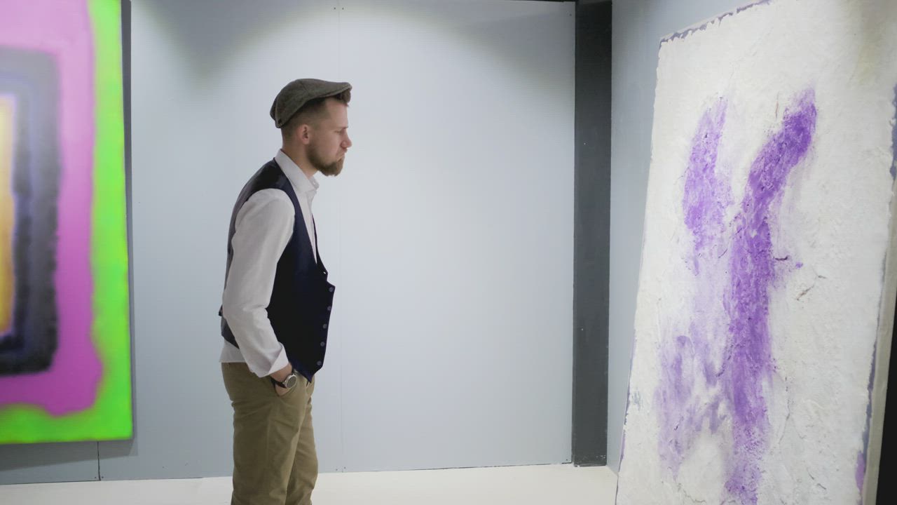 Visitor walking past paintings hanging in an art gallery